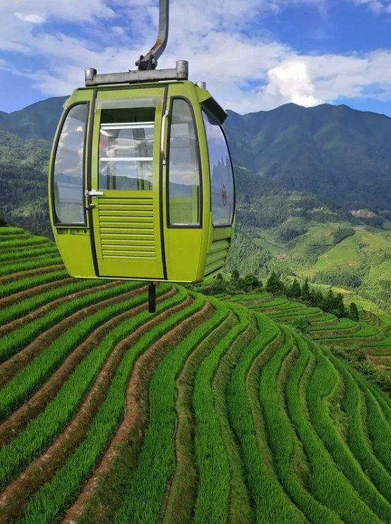 A single green cable-car cabin above the Longji Rice Terraces with mountains and cloud behind