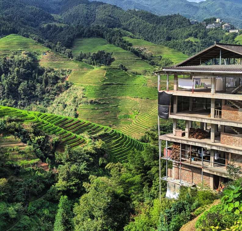 A tall concrete and brick guesthouse with laundry drying on its balconies, built on the edge of the Longji Rice Terraces