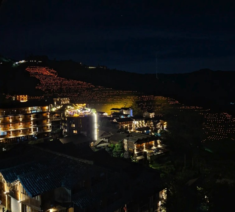 The Longji Rice Terraces picked out by rows of small lamps after dark above a lit village