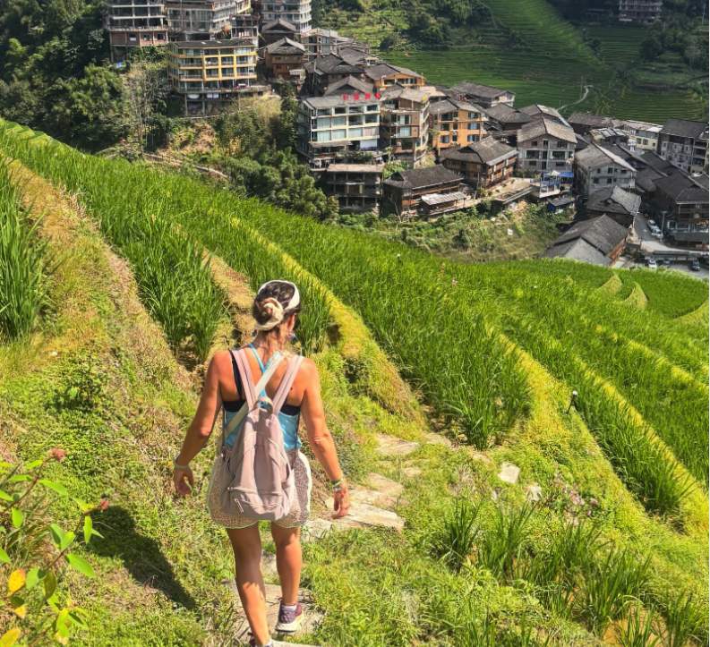 A walker with a backpack descending a stone path through the Longji Rice Terraces towards Ping'an village